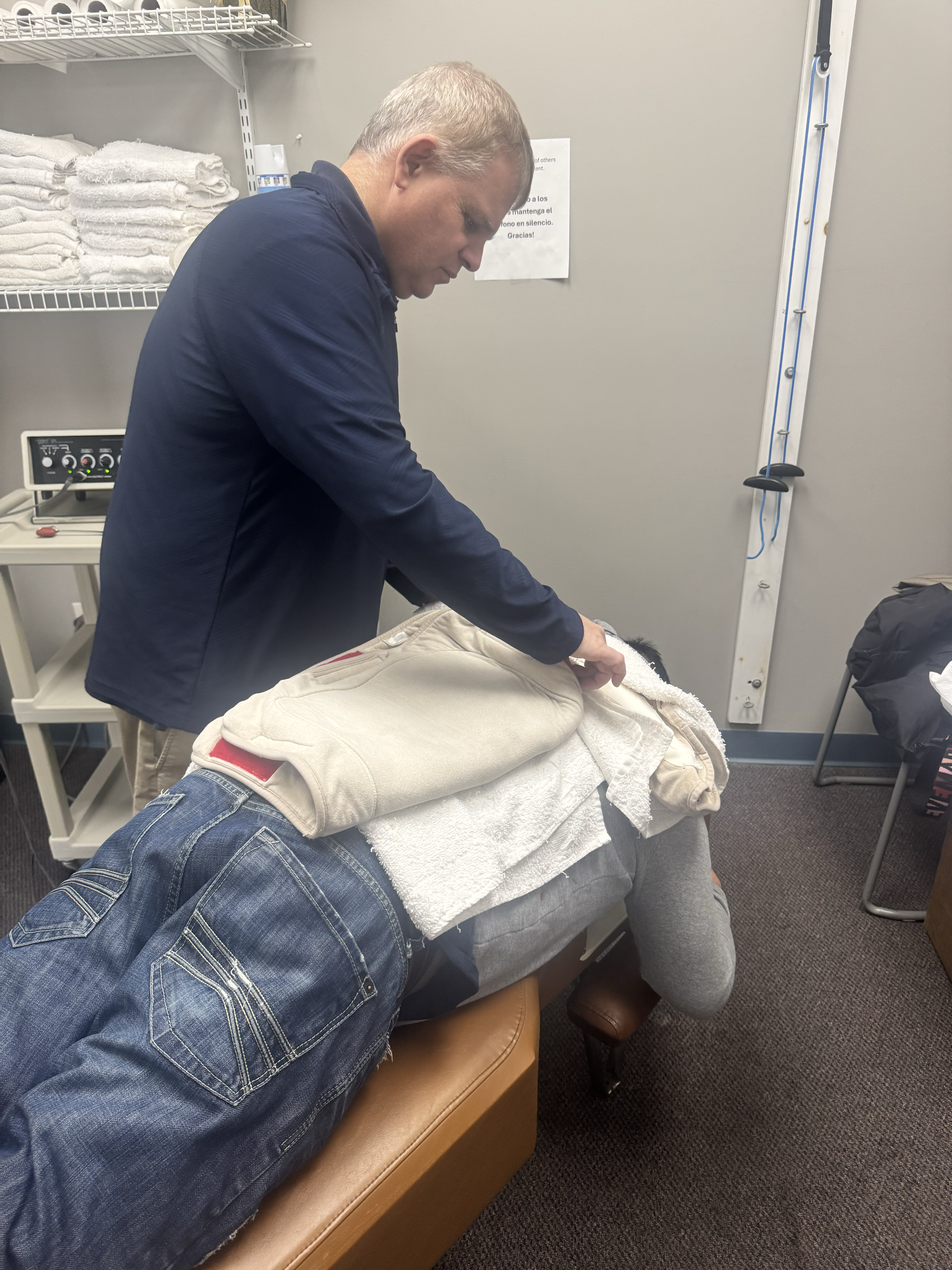 Chiropractor adjusting a patient's neck, who is lying on a table. Setting appears to be a medical office.