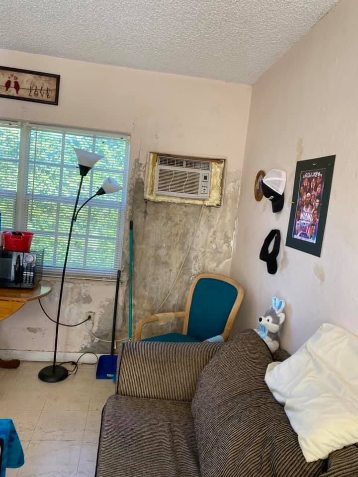 Living room with peeling walls, window AC unit, couch, chair, and decor.