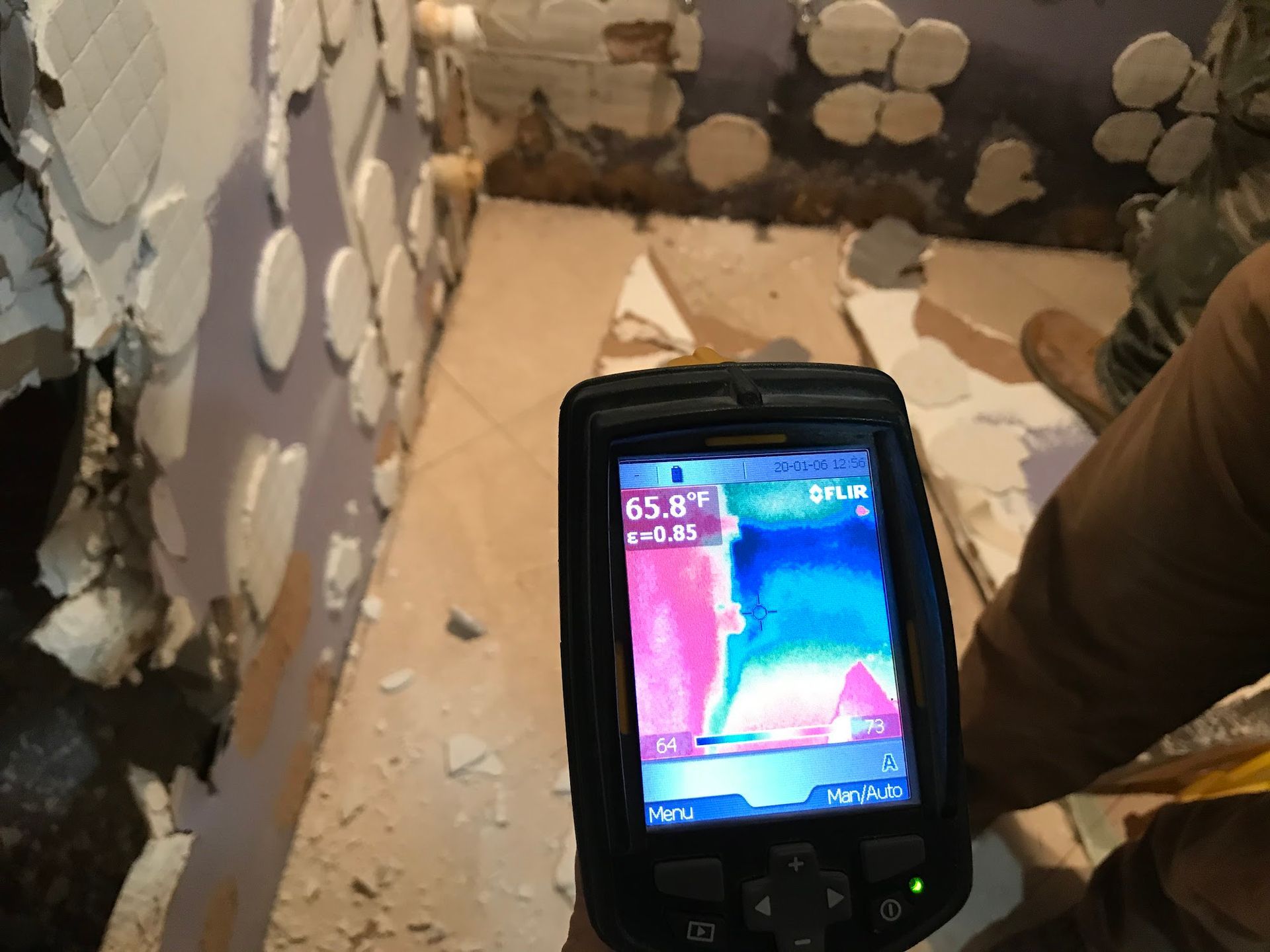 An infrared camera reveals heat differences in a room under construction. The device displays temperature readings in color.