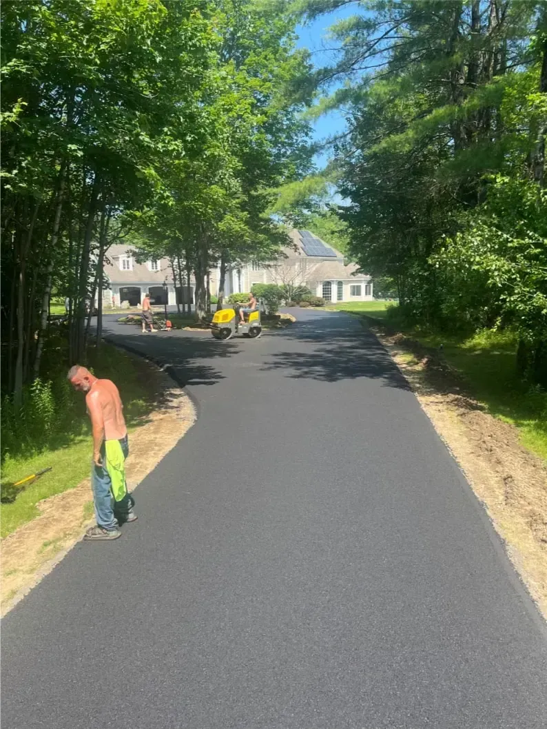 Paved asphalt driveway with worker in neon green, machines, and large house in background.