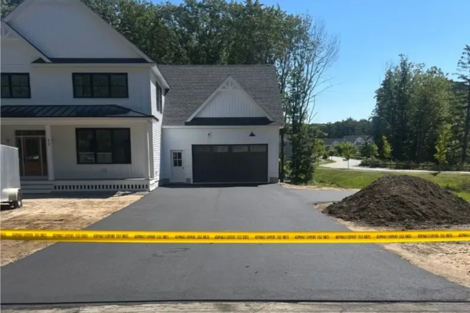 Newly paved asphalt driveway in front of a white house with a garage, with caution tape across the image.