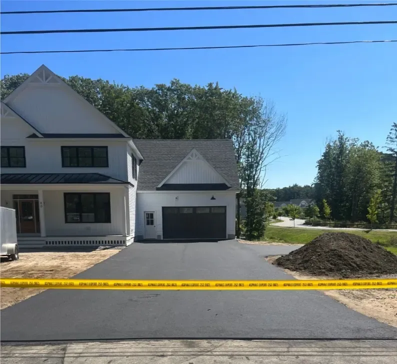 New asphalt driveway in Maine leading to a white two-story house with a garage.