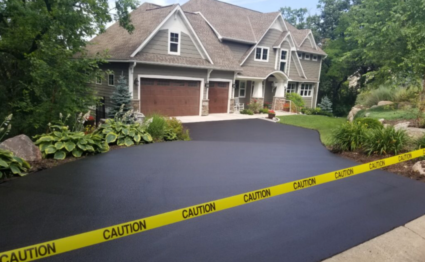 Large suburban house with fresh black driveway sealed off by yellow caution tape