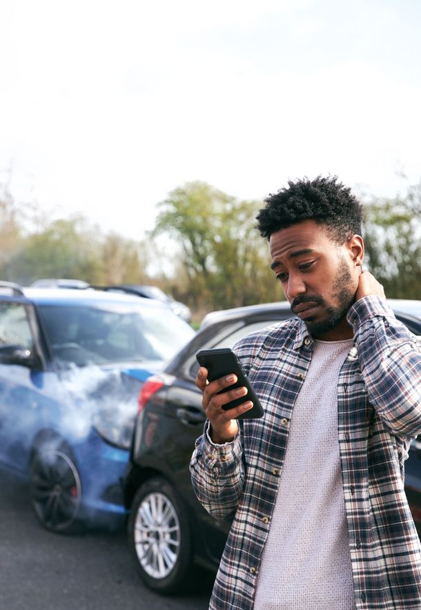 Man checking his phone beside a smoking black car in a parking lot
