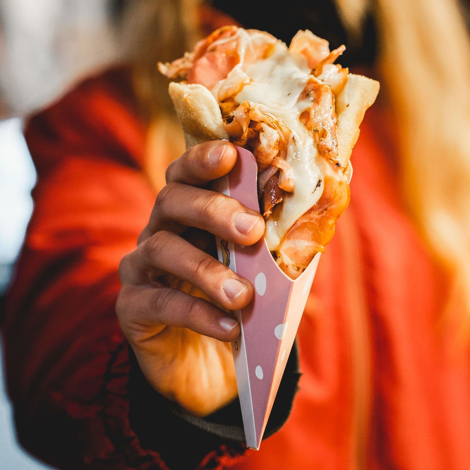 Una mano regge un cono di pizza ripieno di formaggio fuso e salumi,