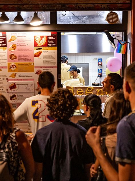 Le persone aspettano in fila davanti a una bancarella di cibo con un menù 