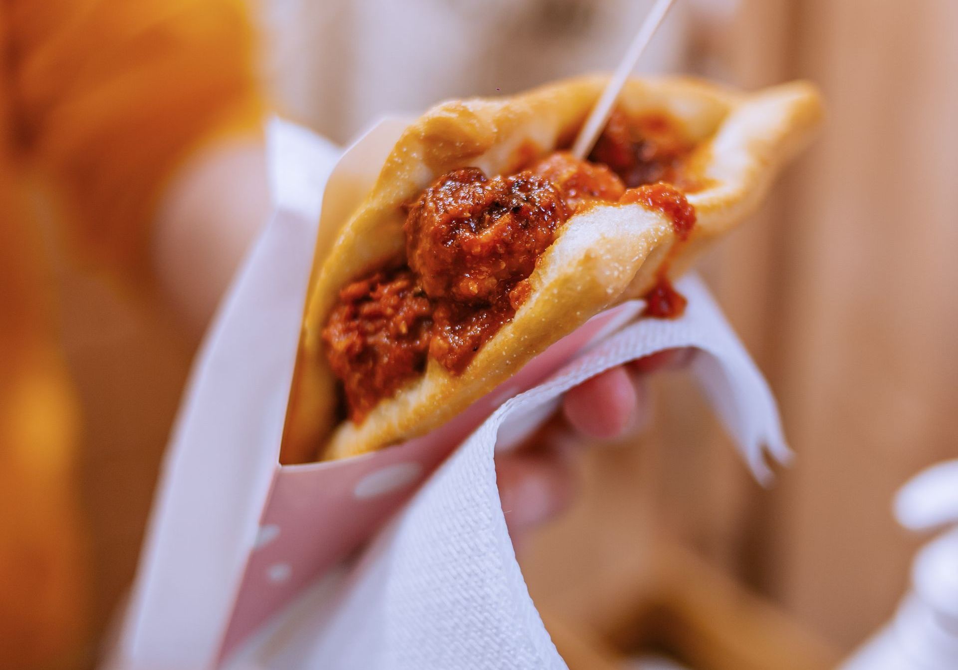 Una persona tiene in mano un pezzo di pasta fritta dorata ripieno di saporito ragù di carne rossa