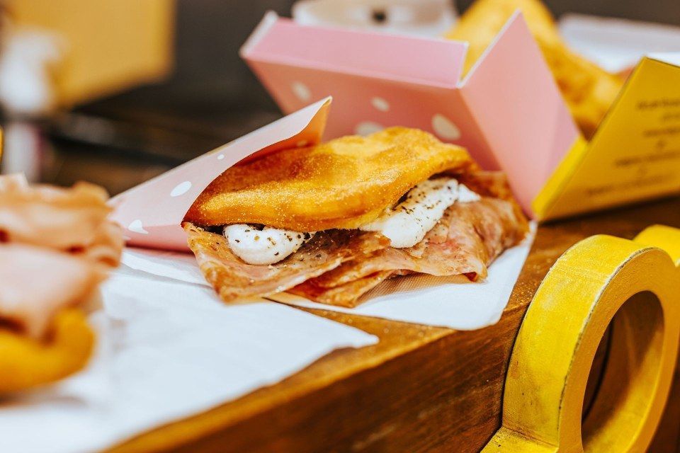 Un panino salato fritto con prosciutto e formaggio morbido, servito in una scatola rosa da asporto su un tavolo di legno.