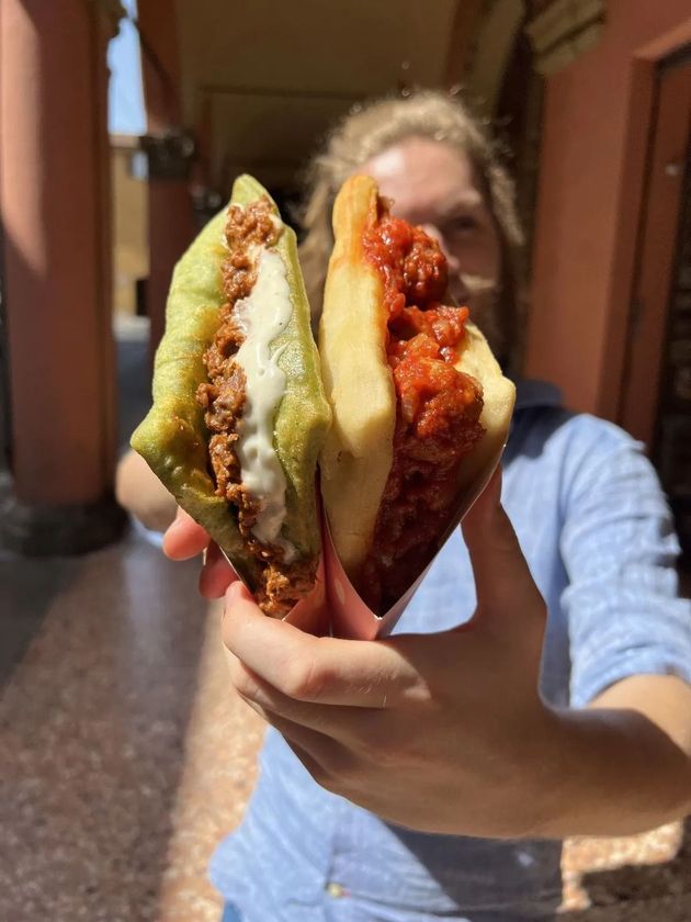 Una persona tiene in mano due panini fritti, uno con carne e formaggio