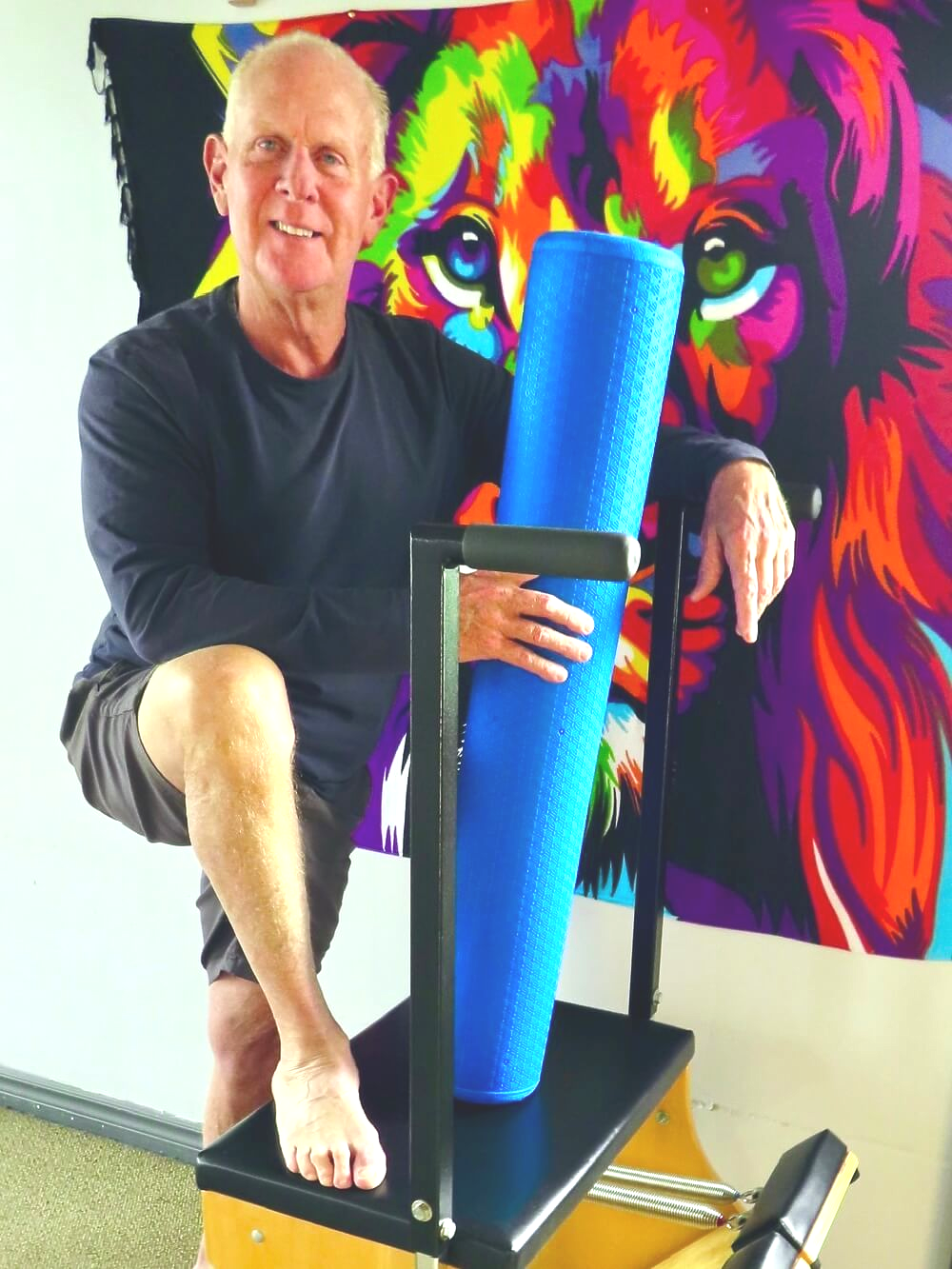 Man seated beside a blue foam roller in front of a colorful lion mural