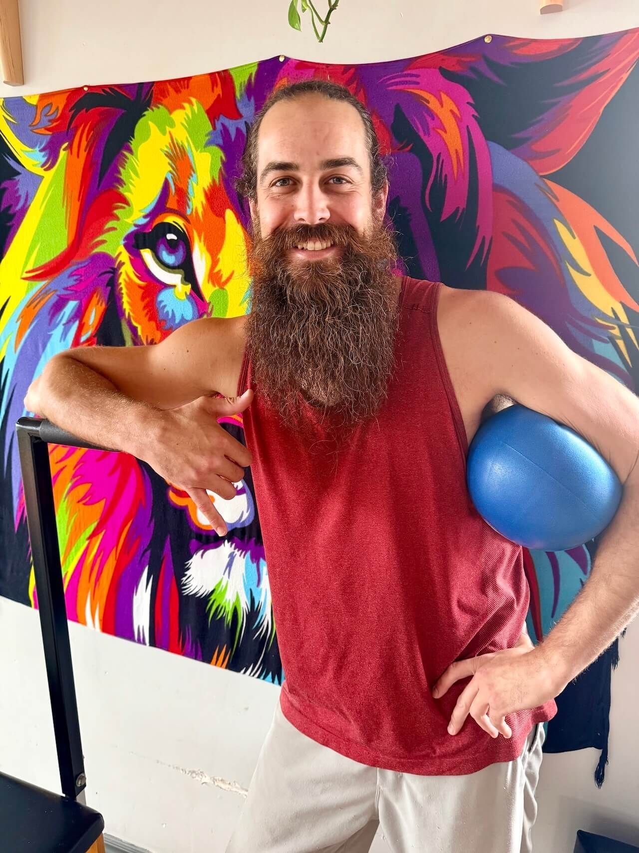 Man posing in front of a colorful lion mural, holding a blue ball against his side.