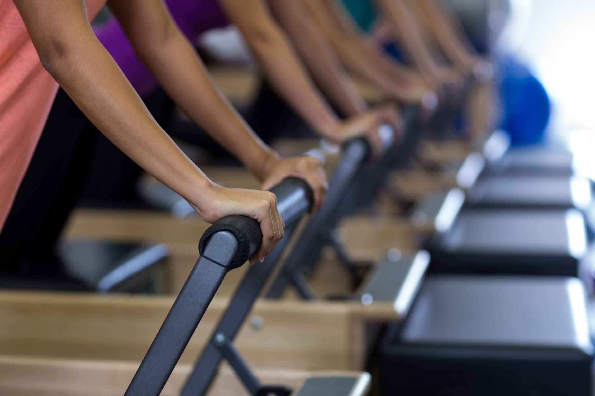 People exercising on rowing machines in a Pilates studio, in a row of reformer equipment