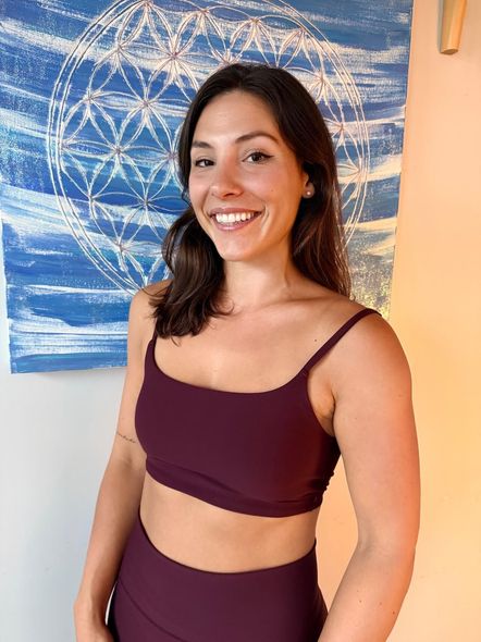 Smiling person in maroon athletic wear standing before a blue abstract wall hanging