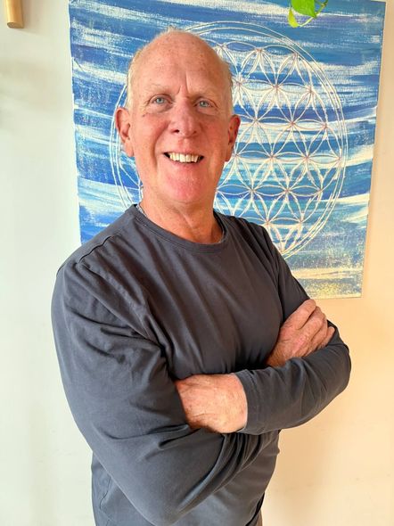 Smiling man in gray shirt with arms crossed, standing before a blue-and-white abstract painting.
