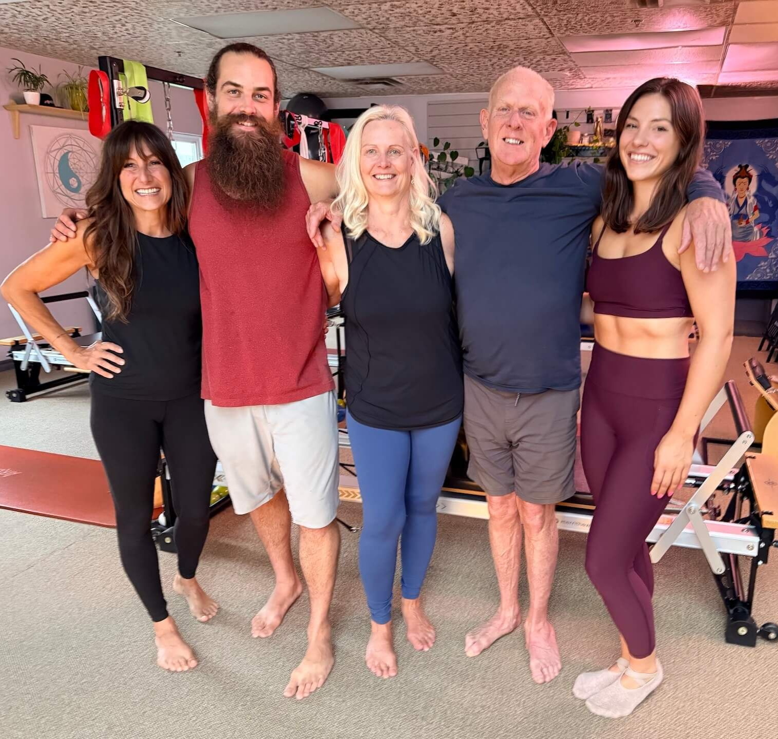 Five people standing barefoot in a gym, smiling in workout clothes.
