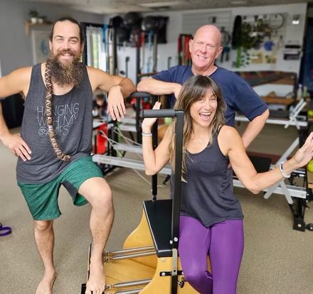Three people posing in a gym, smiling beside exercise equipment.