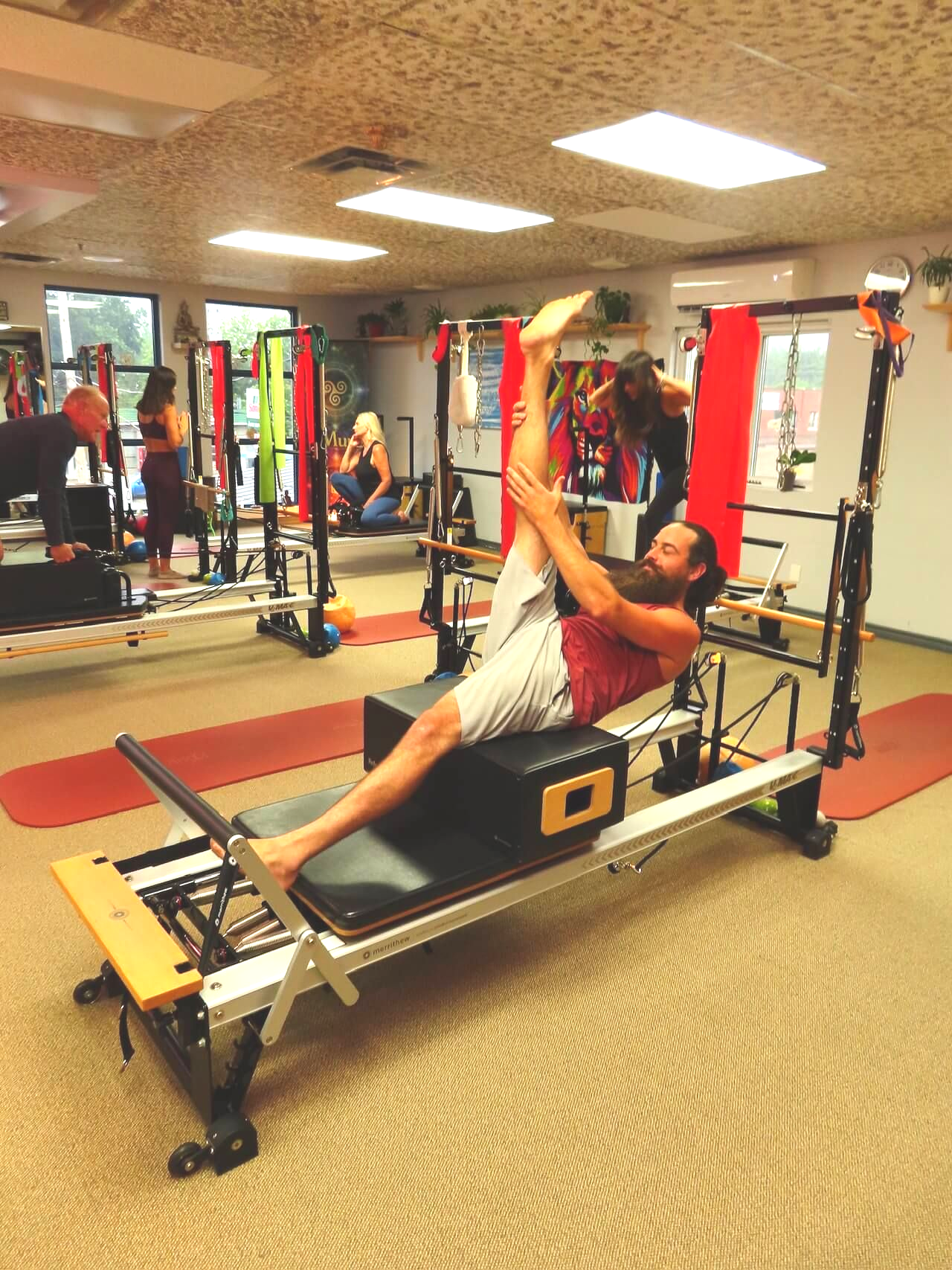 Woman seated on a wooden chair performing a back extension exercise in a bright room with colorful wall art