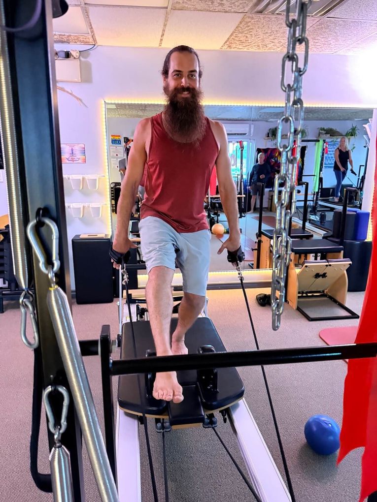 Man walking on a treadmill in a gym, wearing a red shirt and light shorts.
