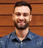 Smiling man in a blue patterned shirt against a wooden wall
