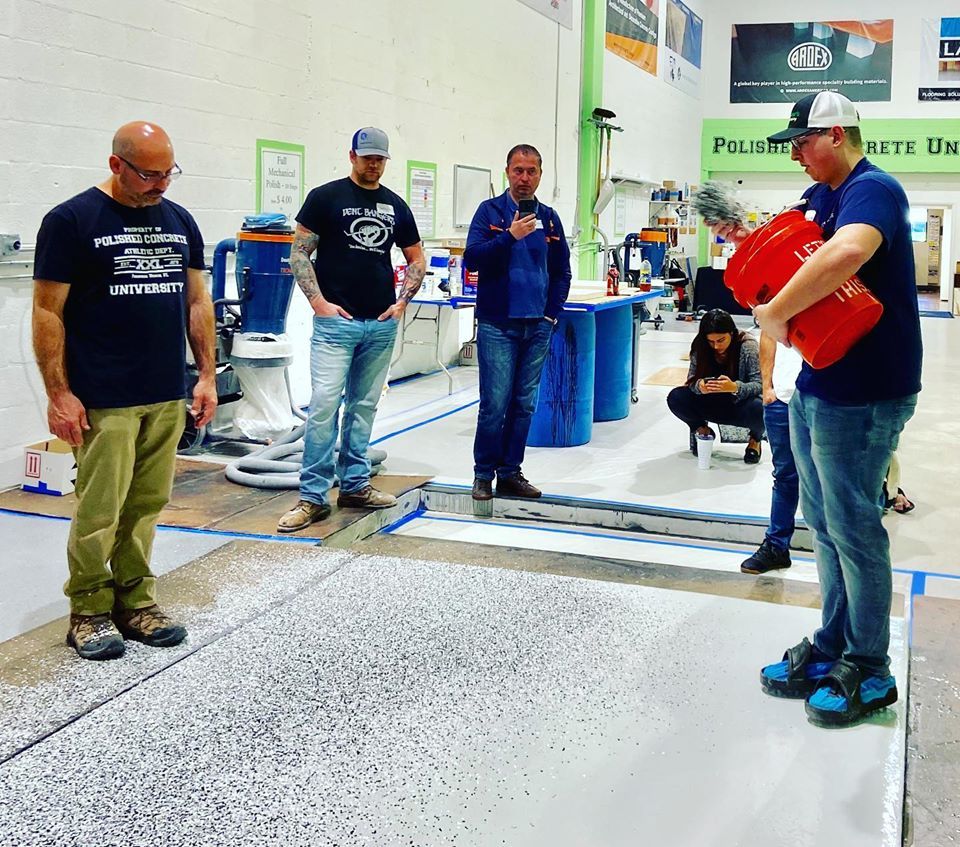 People standing around a marked floor line at an indoor trade show booth, one holding a red item.
