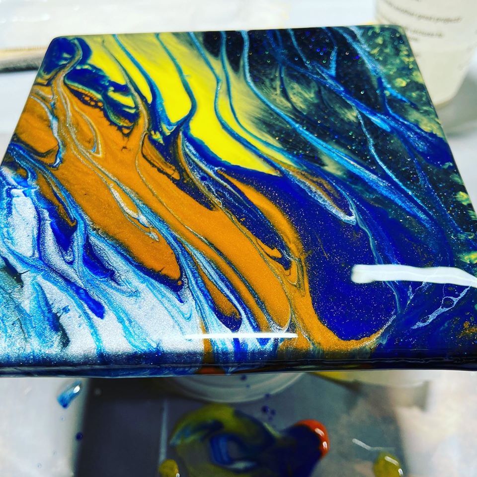 Abstract acrylic pour painting with swirling blue, yellow, orange, and white marbling on canvas