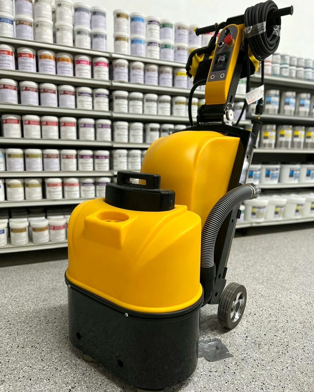 Yellow floor-cleaning machine in a store aisle with shelves of stacked cans in the background