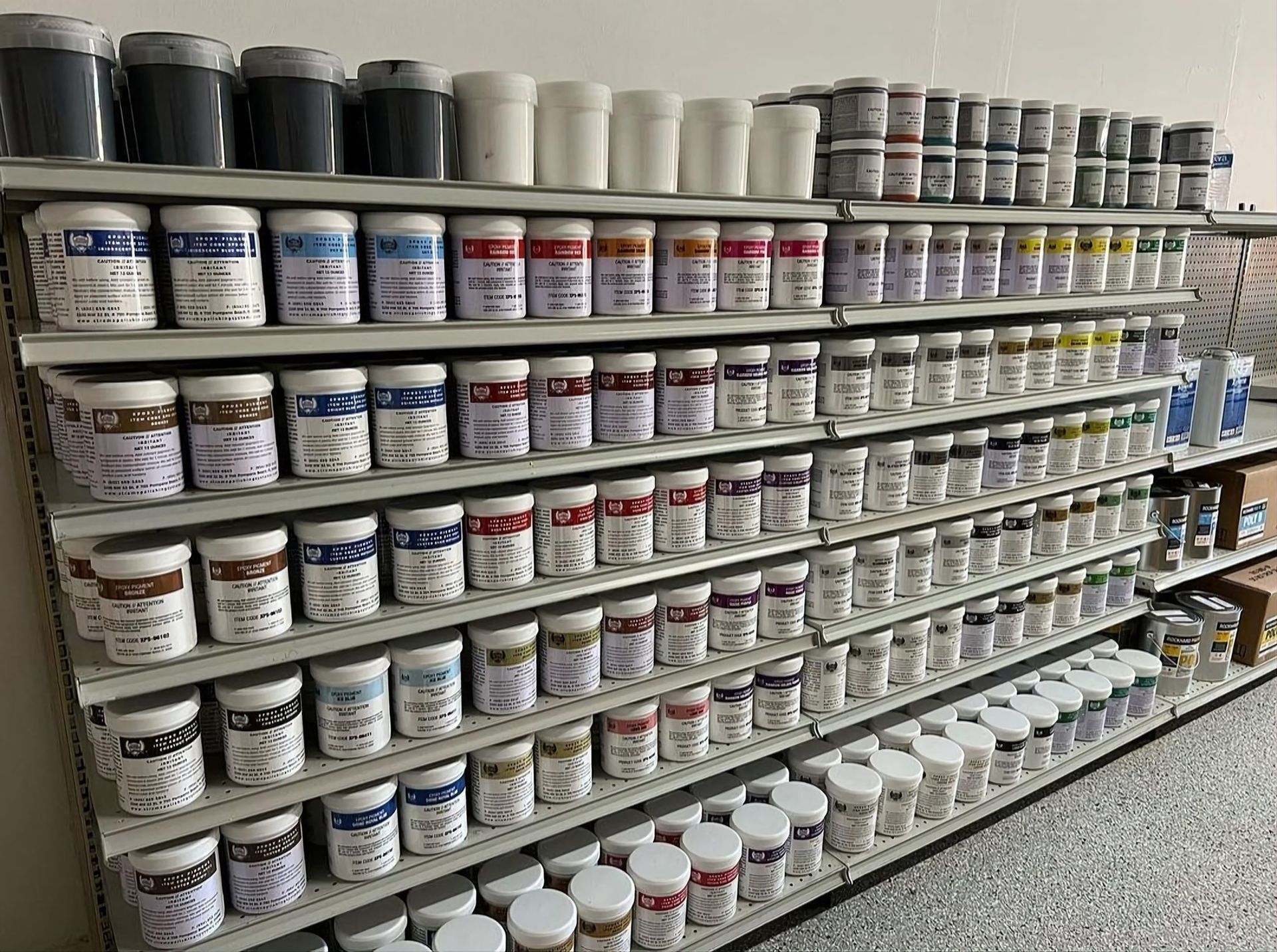 Shelves stocked with rows of paint cans and jars in a hardware store aisle