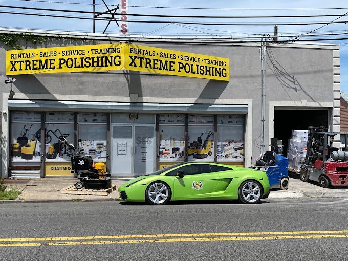 Green sports car parked outside Xtreme Polishing shop with yellow banners and tools in the window