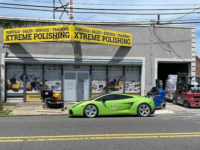 Bright green sports car parked outside Xtreme Polishing auto shop with scooters and workshop equipment nearby