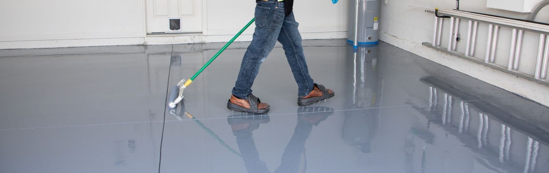 Person mopping a glossy gray floor in a bright hallway with a green-handled mop.
