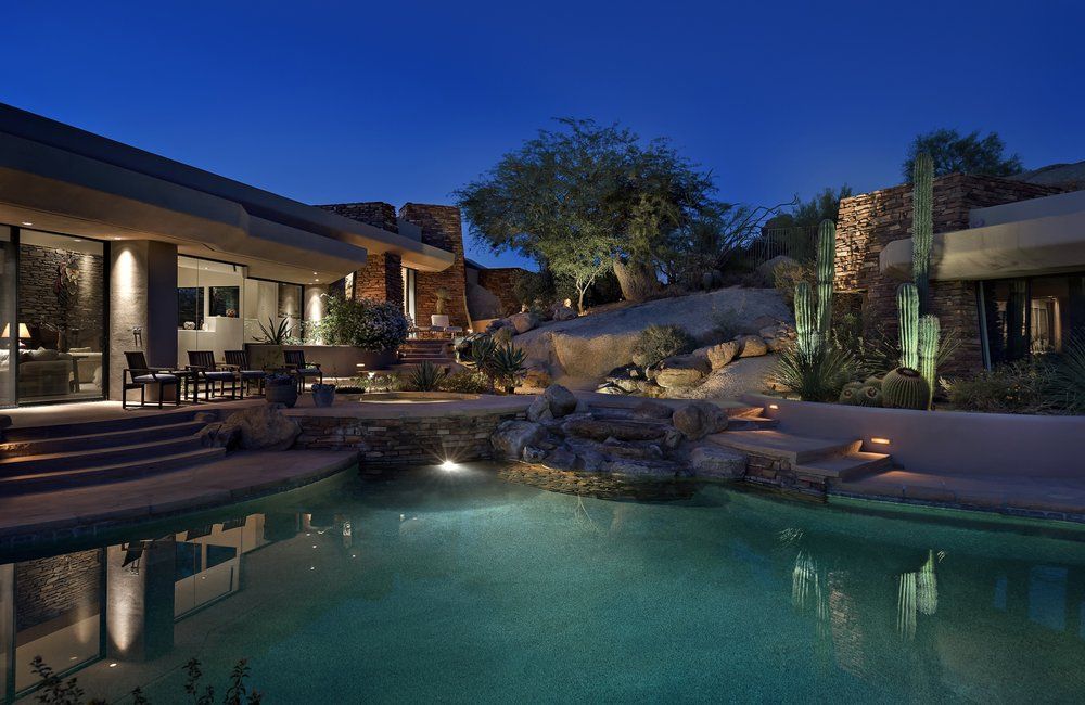 Pool and luxury home at night, with illuminated water features and desert landscaping.