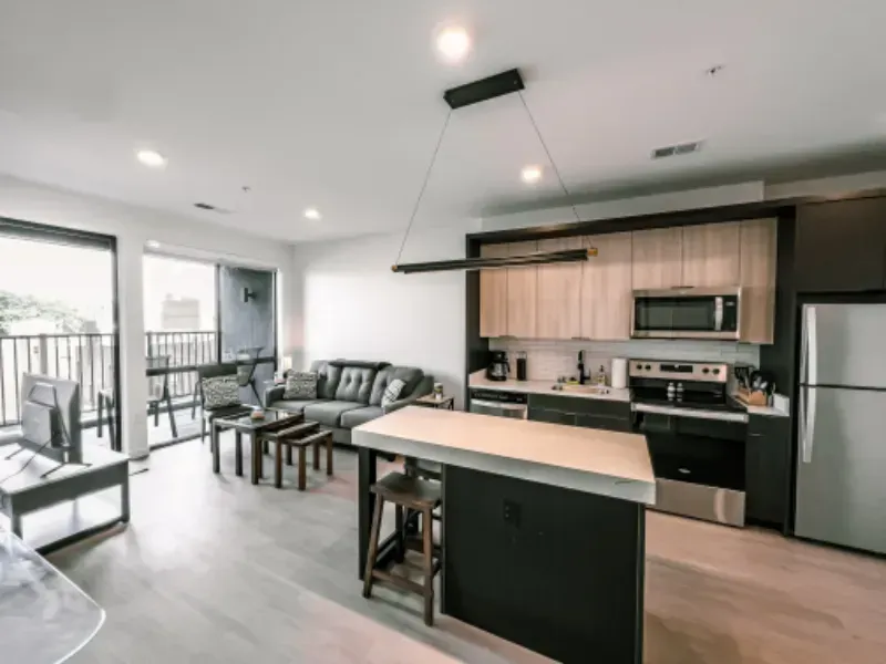 A modern, open-concept kitchen and living area featuring a central island, stainless appliances, and a gray sofa.