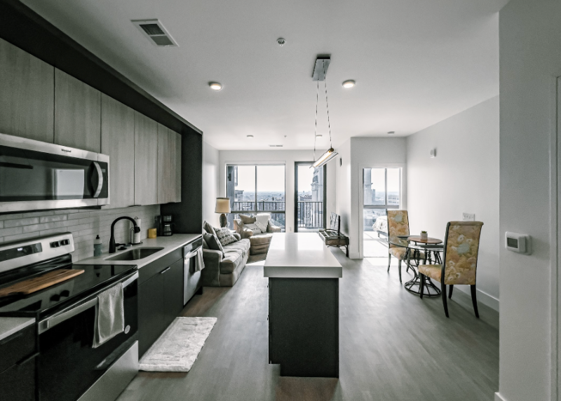 Modern kitchen and living space featuring a central island, stainless appliances, gray cabinetry, and a dining area.