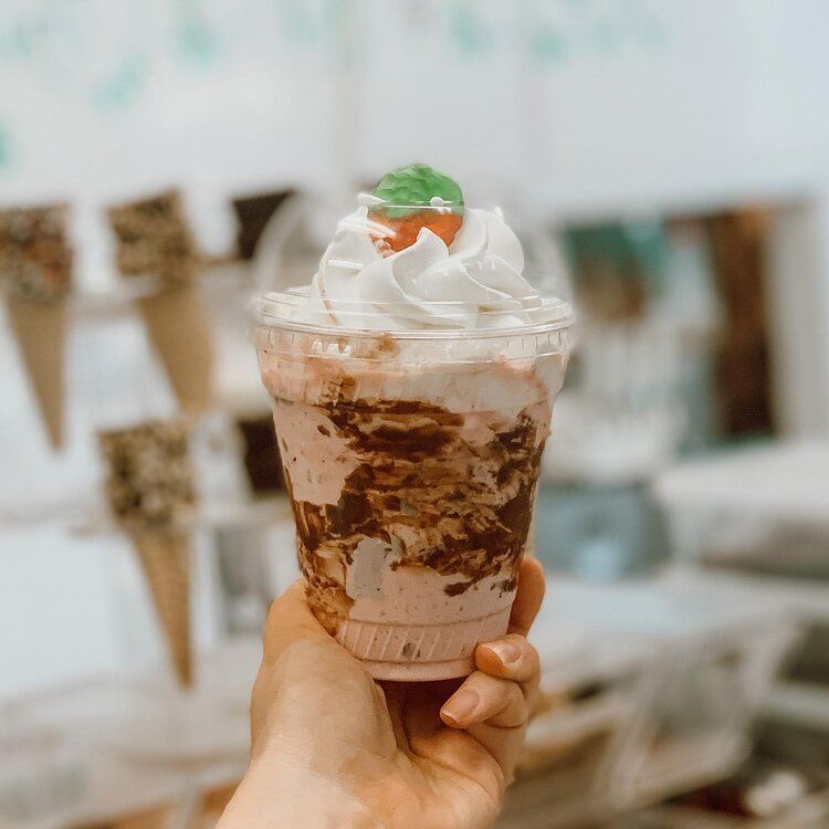A person is holding a cup of ice cream with whipped cream and a strawberry on top