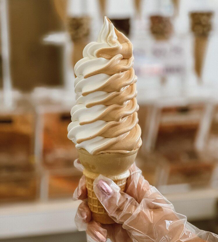 A person wearing plastic gloves is holding a soft serve ice cream cone.