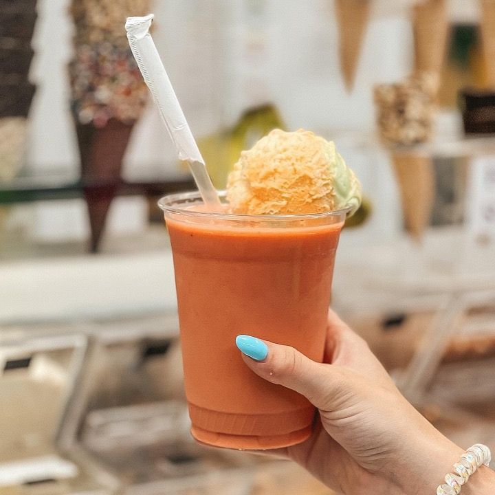 A person with blue nails is holding a smoothie with ice cream in it