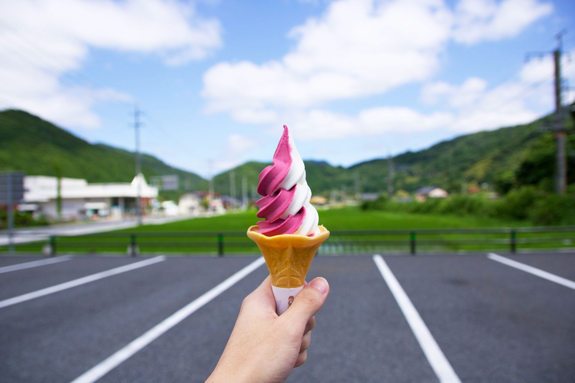 A person is holding a purple and white ice cream cone in a parking lot.