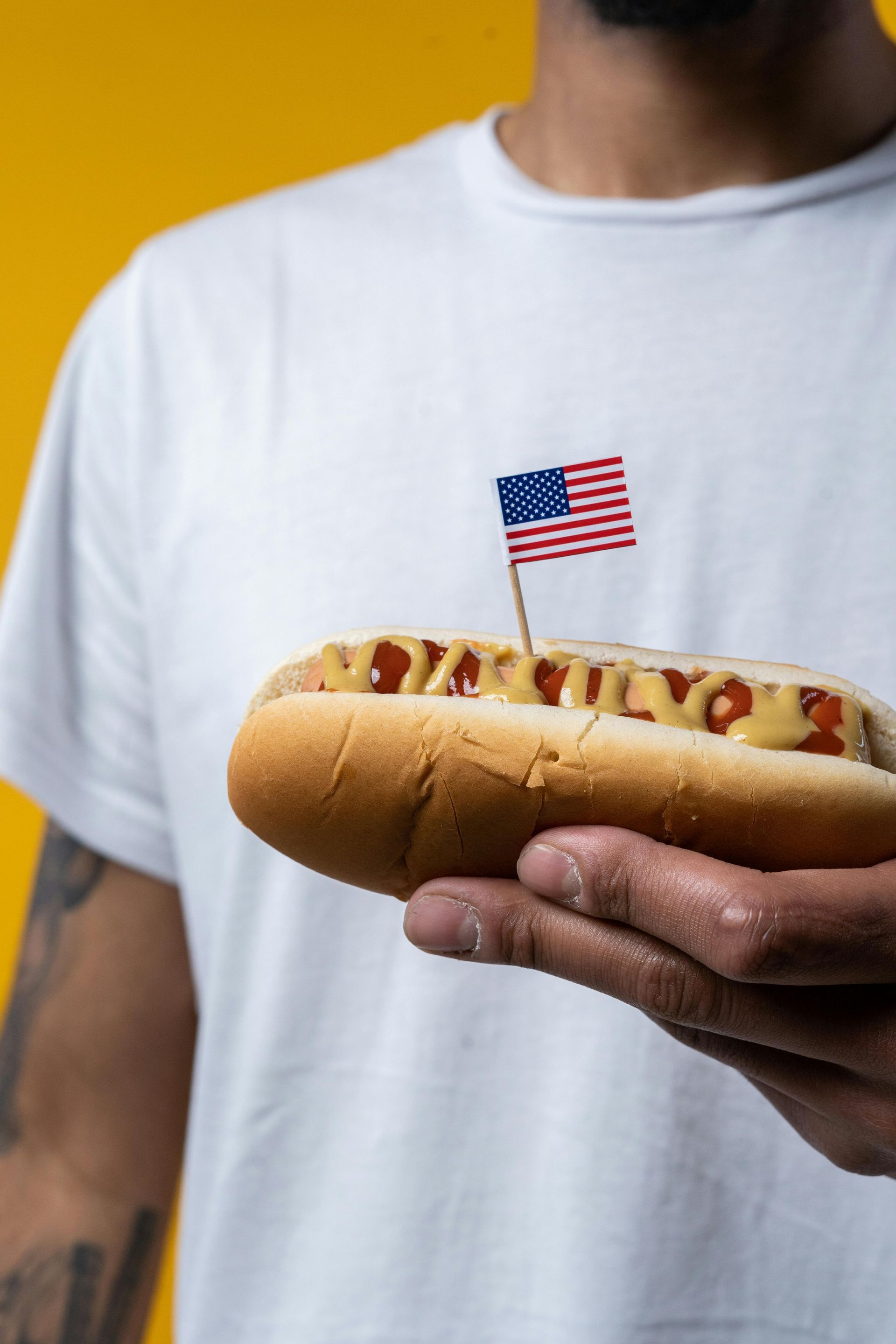 A man is holding a hot dog with a small american flag sticking out of it.