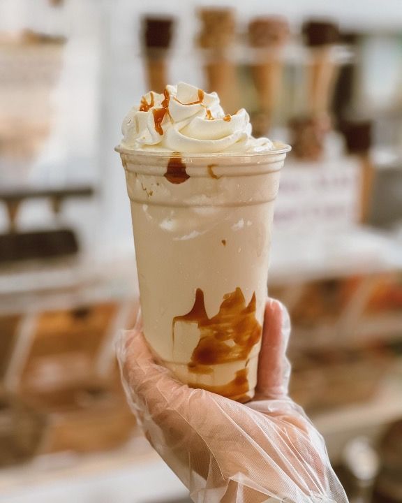 A person is holding a cup of ice cream with whipped cream and caramel sauce.