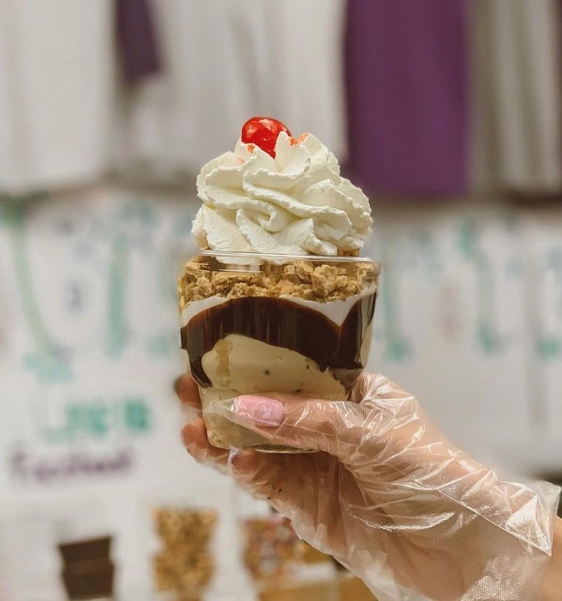 A person is holding a cup of ice cream with whipped cream and a cherry on top.