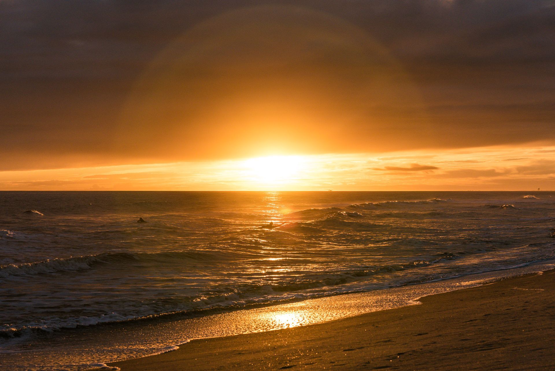Sunset over the ocean with golden light reflecting on gentle waves and a sandy shoreline