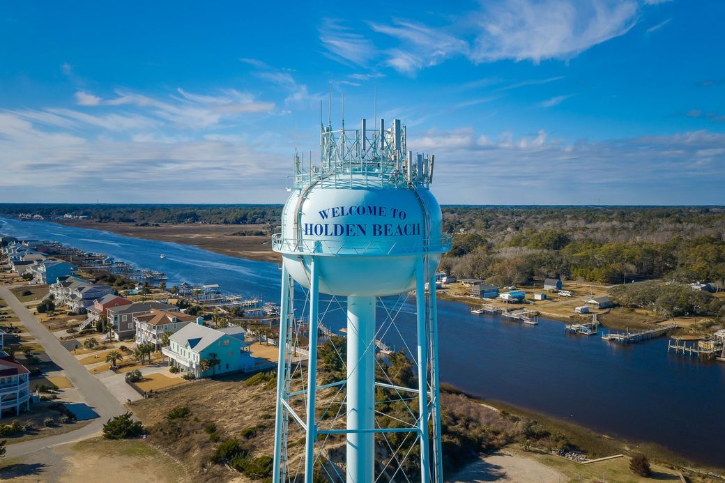 Blue water tower over a river and bridge in a coastal town under a bright blue sky