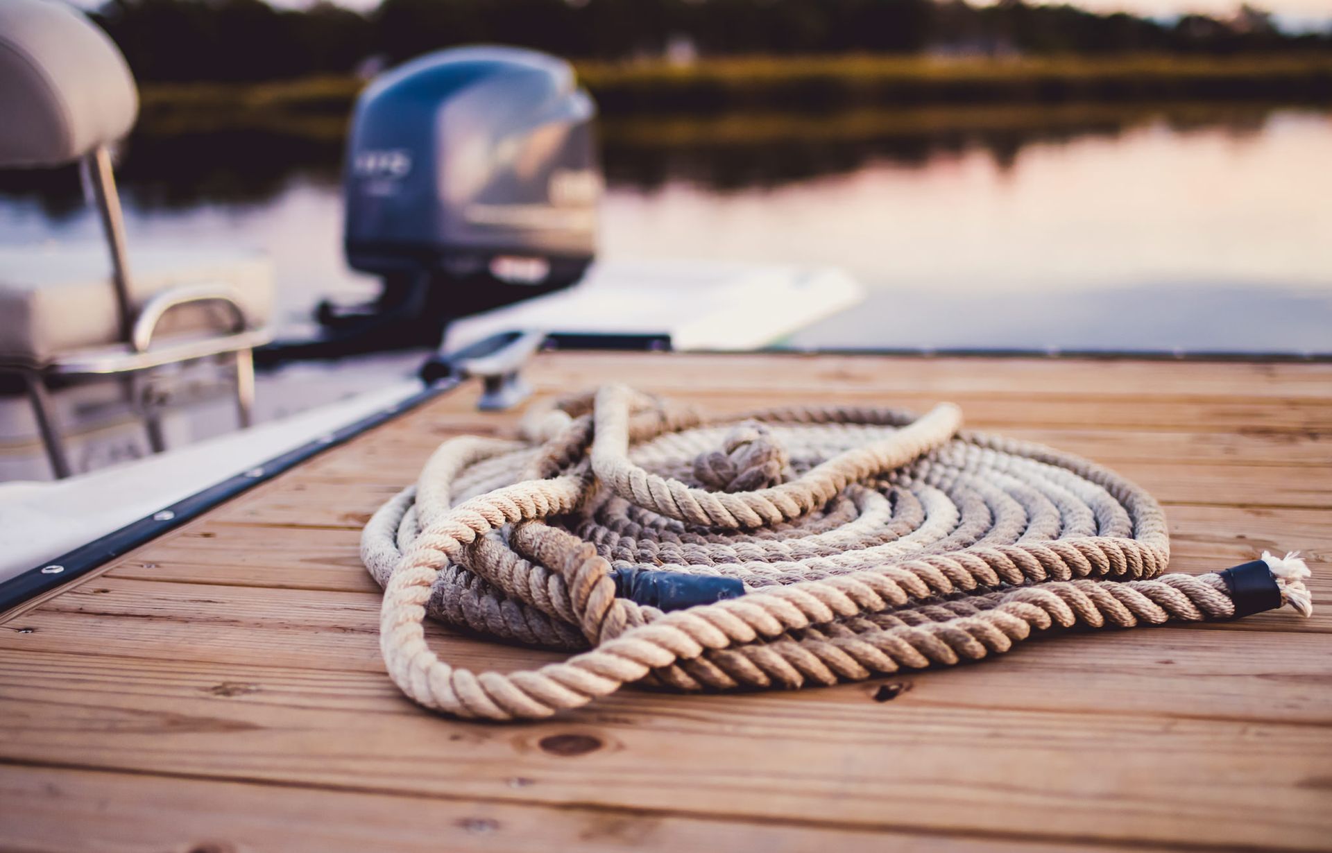 Coiled rope on a wooden dock beside a lake at sunset, with a boat in the background