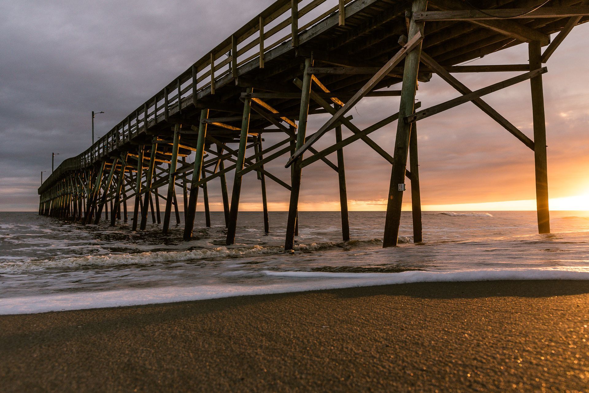 Long wooden pier over choppy water at sunset, with waves breaking on the shore