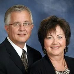 Studio portrait of two professionally dressed people smiling against a blue backdrop