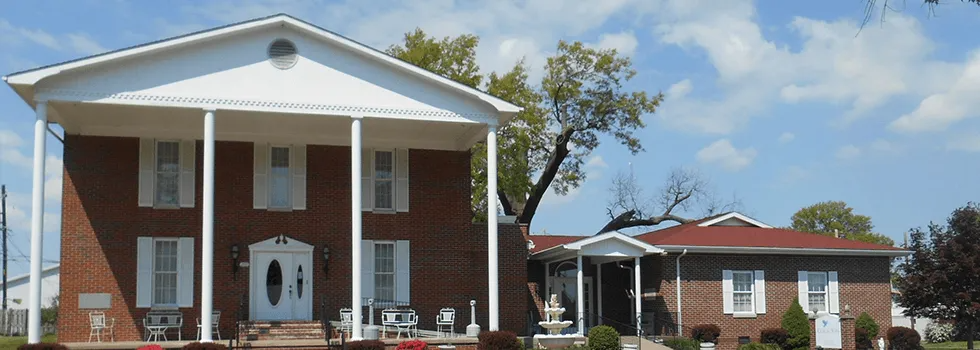 Brick civic building with white columns and a blue-roofed annex under a clear sky