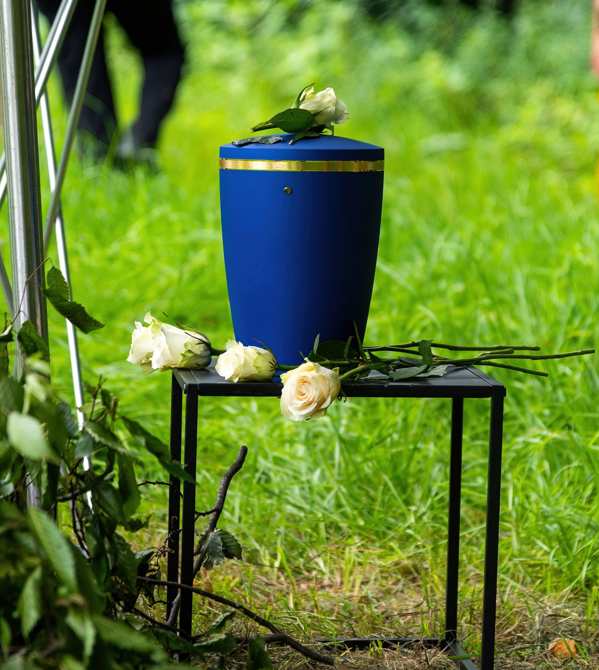 Blue urn on black stand with white flowers in green grass outdoors