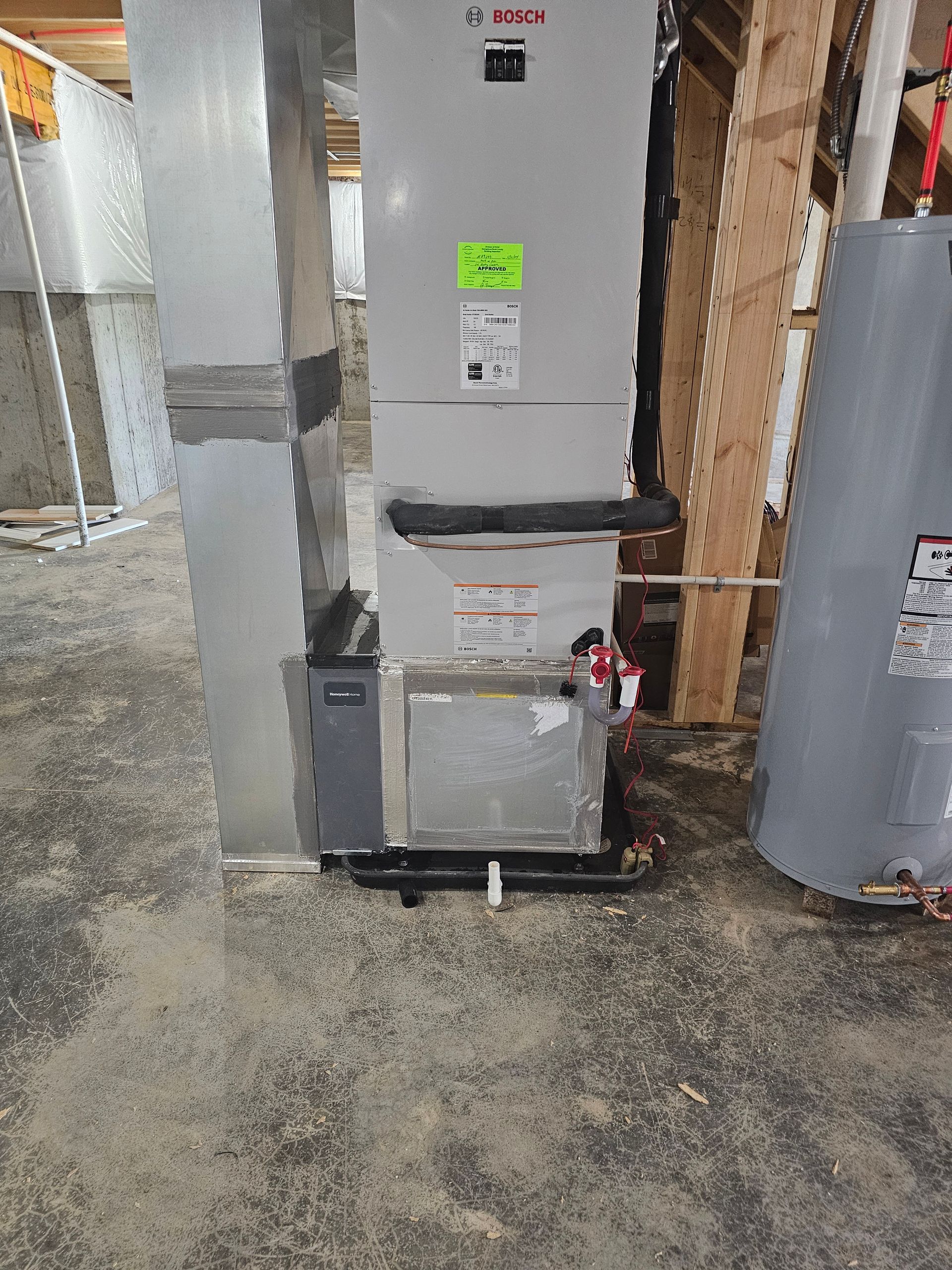 A water heater is sitting next to a heater in a basement.
