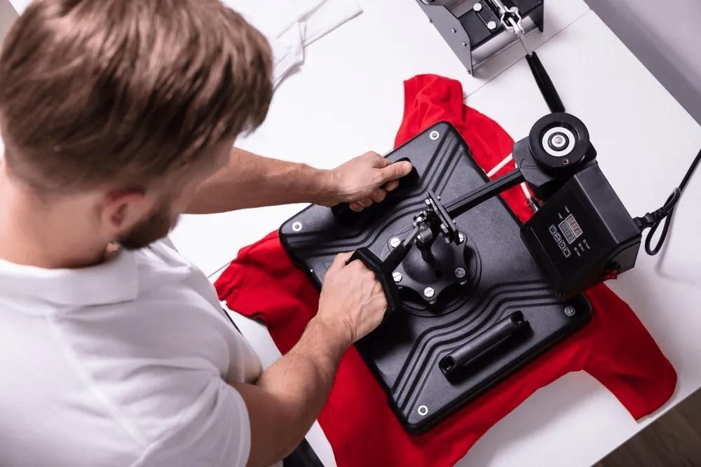 A Man Is Using a Heat Press Machine to Print a Red Shirt — Imsprint in Lake Macquarie, NSW