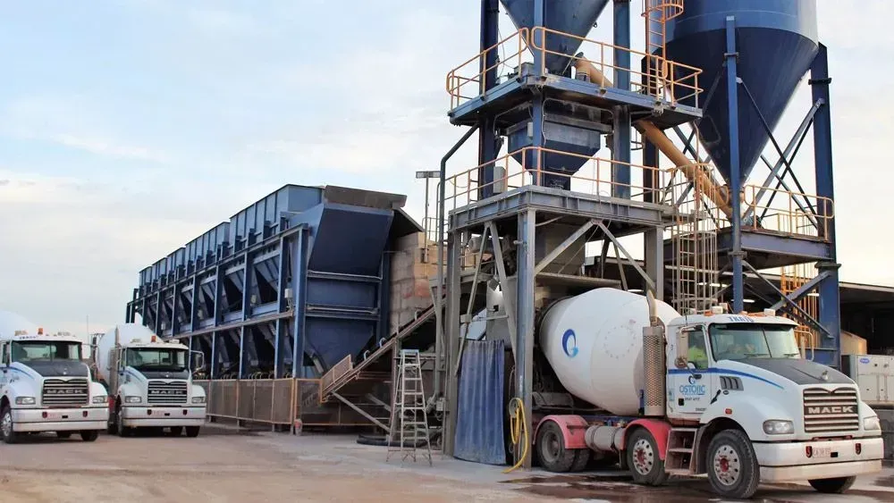 Concrete batching plant with large industrial silos and mixer trucks parked on-site